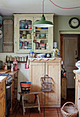 Glass fronted cabinet and bucket on stool in small Somerset kitchen, UK