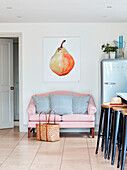 Large artwork of a pear above pink two seater sofa in Oxfordshire kitchen, UK