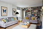 Schmetterlingsdrucke und Sofas mit Bücherregal in einem Wohnzimmer in Oxfordshire, UK