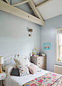 Kissen und Decken auf dem Bett in einem hellblauen Mädchenzimmer mit Balkendecke Oxfordshire, UK