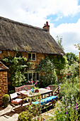 Terrassenmöbel vor einem traditionellen reetgedeckten Cottage in Oxfordshire, UK