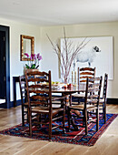 Dining table and chairs with patterned rug and artwork of ram in North Yorkshire farmhouse, UK