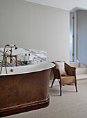 Wicker chair and freestanding bath with marble splashback in North Yorkshire farmhouse, UK