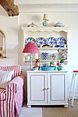 Decorative plates on shelves above cupboard with gingham lamp in, UK cottage
