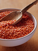 Dish of raw red lentils with wooden spoon