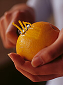 Hände halten eine Orange und benutzen einen Zestenreißer