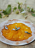 Sliced oranges with cinnamon and icing sugar garnished with sprigs of mint