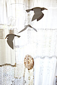 Three paper birds fly against sunlit lace curtains in Brighton home East Sussex, England, UK