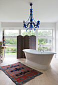 Freestanding bath and patterned rug with folding screen at window in Guildford home, Surrey, UK