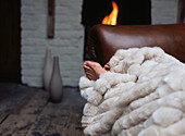 Person under a blanket on a sofa next to a lit open fire in the living room