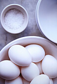 Nahaufnahme einer Schale mit weißen Eiern und Salz in einer kleinen Tasse auf einer weißen Marmorarbeitsplatte