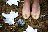 Nahaufnahme einer Frau mit goldenen Schuhen, die auf einem Waldboden mit silbernen Blättern steht