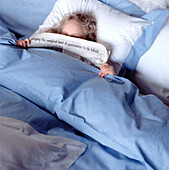 Young girl laying in a double bed with newspaper