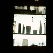 Blick aus dem Fenster eines Schuppens mit Schatten von Farbtöpfen und Heimwerkerprodukten auf Regalen