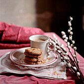Tasse Tee und Teller mit einem Stapel selbstgebackener Kekse auf rosa Tischtuch