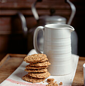 Pile of homemade biscuits on a country style wooden tabletop with a white jug and vintage kettle