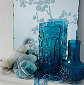 Detail of turquoise blue glass vases and homeware on a shelf with an etched mirror on the wall