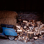 Ein Moped mit Holzstapel und ein Heustapel in einer alten Backsteinscheune