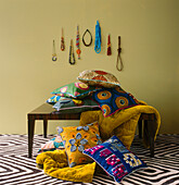 patterned fabric and cushions piled on a tabletop with patterned carpet and a display of necklaces