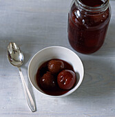 Homemade fruit preserves glass storage jar and a bowl of preserved plums
