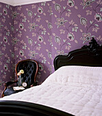Bedroom with brightly coloured patterned wallpaper ornate black double bed with white bed linen