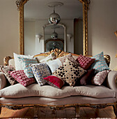 Decorative upholstered vintage sofa piled with patterned fabric cushions in a living room with large mirror