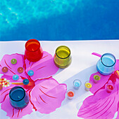 Coloured glass candle holders on a table in the garden next to a swimming pool