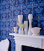 Blue bold patterned wallpaper in a living room with white painted fire surround and white home wares