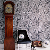 Bold patterned wallpaper in a hallway with grandfather clock upholstered chair shoes suitcase and disco balls