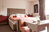 Buttoned headboard with two seater sofa and desk in contemporary bedroom of London home England UK