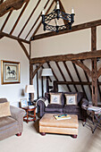 Two seater sofa with leather ottoman in beamed living room of Surrey barn conversion England UK