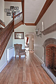 Exposed brick fireplace and wooden banister in hallway with wooden floorboards in Surrey home England UK