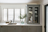 Glass fronted cabinet and leaf arrangement with closed shutters in London kitchen UK