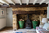 Antique metal log storage in stone fireplace with low beamed ceiling in Cirencester farmhouse Gloucestershire UK