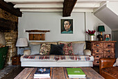 Sofa mit Decke und Kissen und antiker Kommode in einem Bauernhaus in Cirencester, Gloucestershire, Großbritannien