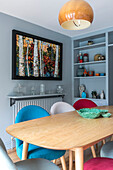 Multicoloured chairs at dining table in light blue room with artwork and shelves Farnham home UK