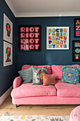 Pink sofa in dark living room with vibrant framed prints in Guildford cottage Surrey UK