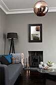 Metallischer Lampenschirm im Wohnzimmer mit Holzbrenner und grauem Sofa