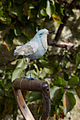 Handmade fabric bird perched on spade handle in walled garden, St Lawrence, Isle of Wight, UK