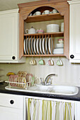 Tellergestell und Abtropffläche mit gestreiftem Stoff unter der Spüle in einem Haus in East Cowes, Isle of Wight, Vereinigtes Königreich