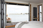 Doppelbett mit Blick durch offene Flügeltüren auf das Meer vom Hausboot in Bembridge, Isle of Wight, Großbritannien