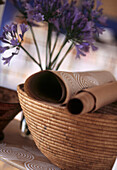 Stilleben von blauen Alliumblüten mit geflochtenem Korb und Rollen von gemustertem Papier