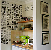Corner of kitchen with open shelves filled with kitchenware and wall decorated with family portraits