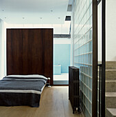 Schlafzimmer mit Kopfteil aus dunklem Holz und eigenem Bad mit blauen Mosaikfliesen in einem umgebauten Industriekeller