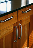 Cherry wood kitchen unit detail with black granite worktop and metal handles