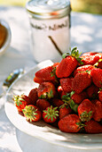 Schale mit frischen, ganzen, roten Erdbeeren auf einem Gartentisch mit Zuckerdose im Hintergrund