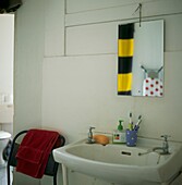 Tableaux in white bathroom of metal stacking chair with reflections in mirror above hand basin