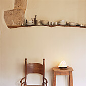 Glazed ceramics displayed on wooden beam in plastered wall above wooden armchair and stool