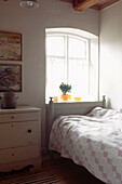 Small white modern country style single bedroom with bed chest of draws and arched window