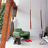 A green 60's armchair with indoor trapeze next to the sloping glass picture window of modern terrace conversion